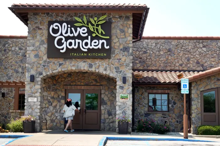 Person entering an Olive Garden restaurant, which features a stone facade and brand signage above the entrance