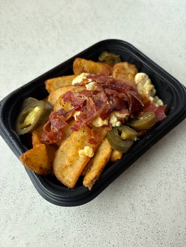 Wendy's jalapeño breakfast potatoes with bacon, cheese sauce, and jalapeños in a black tray on a flat surface